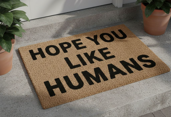 An image of an outdoor entryway rug with the text "HOPE YOU LIKE HUMANS".